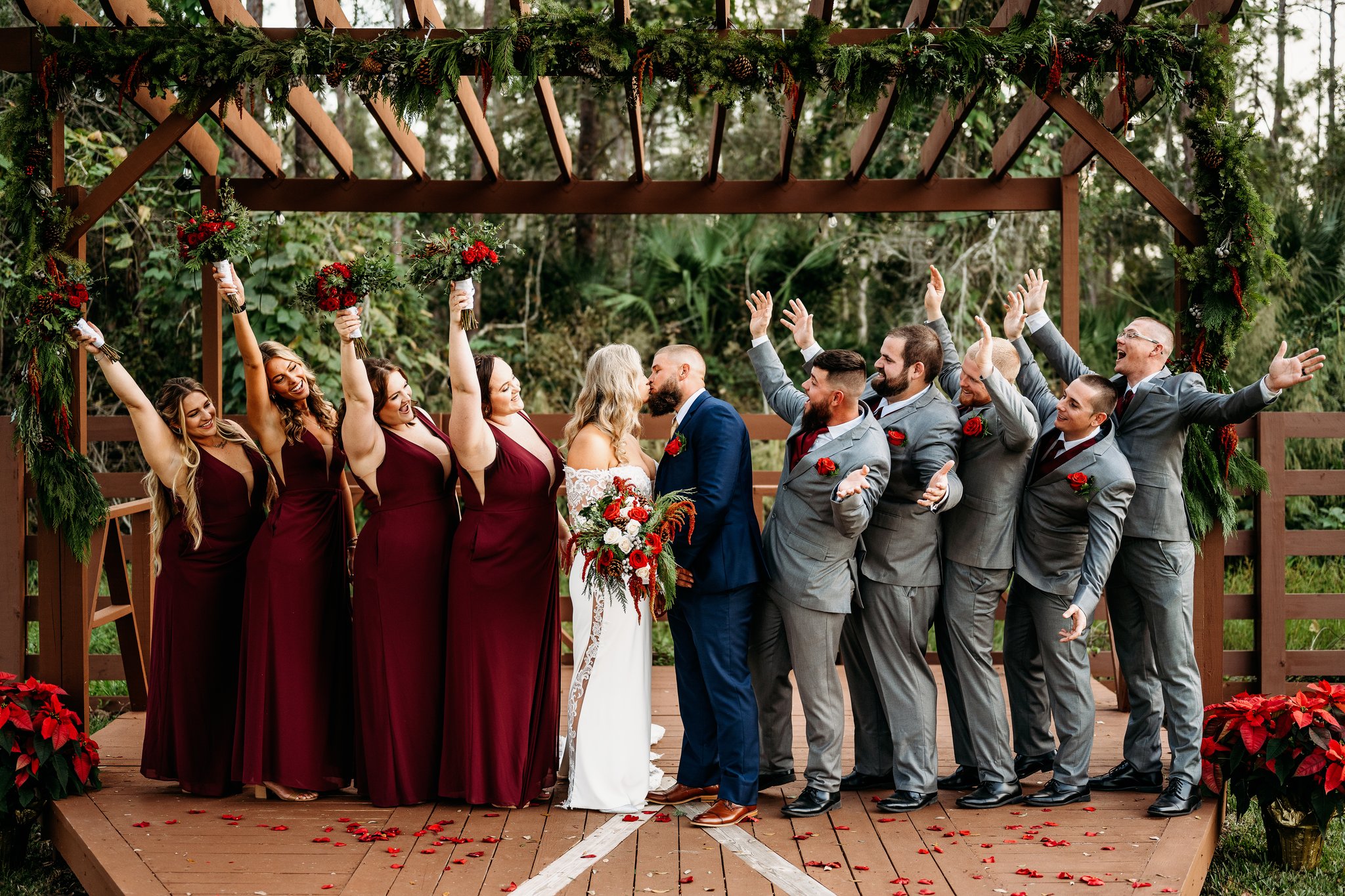 Wedding party celebrating as a couple kisses beneath the ceremony pergola