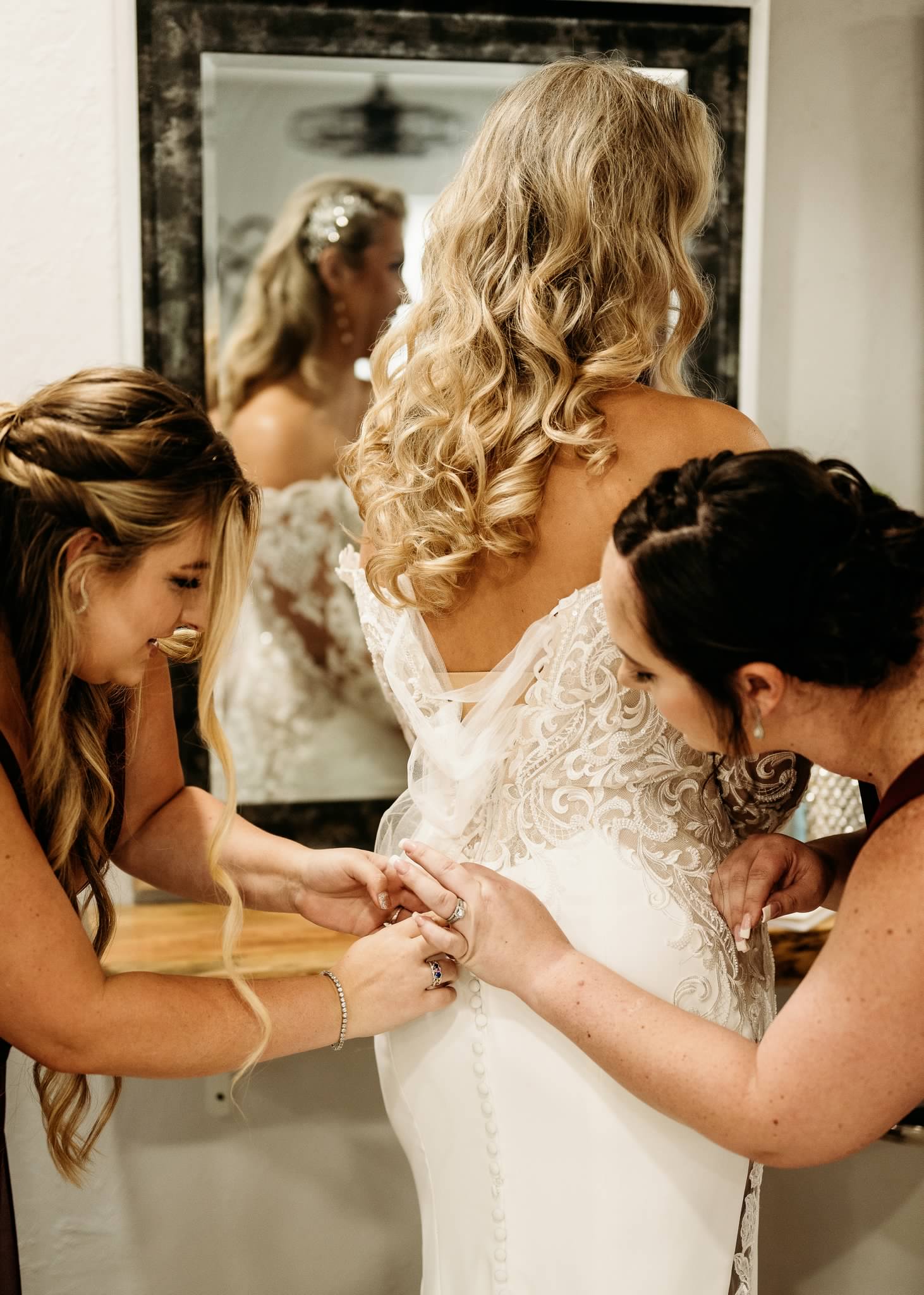 Bridesmaids fastening the bride's gown in the on-site suite