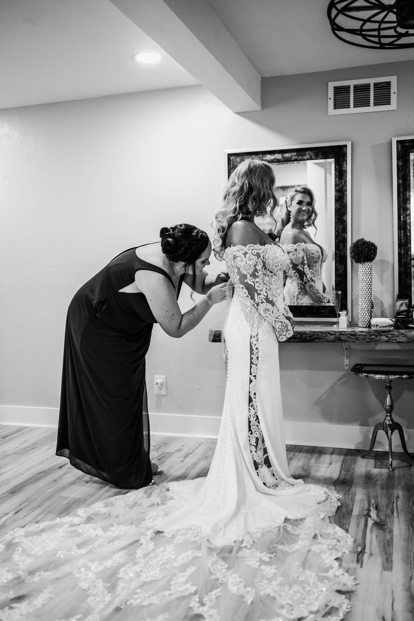 Bridesmaid buttoning the bride's gown before the suite mirror